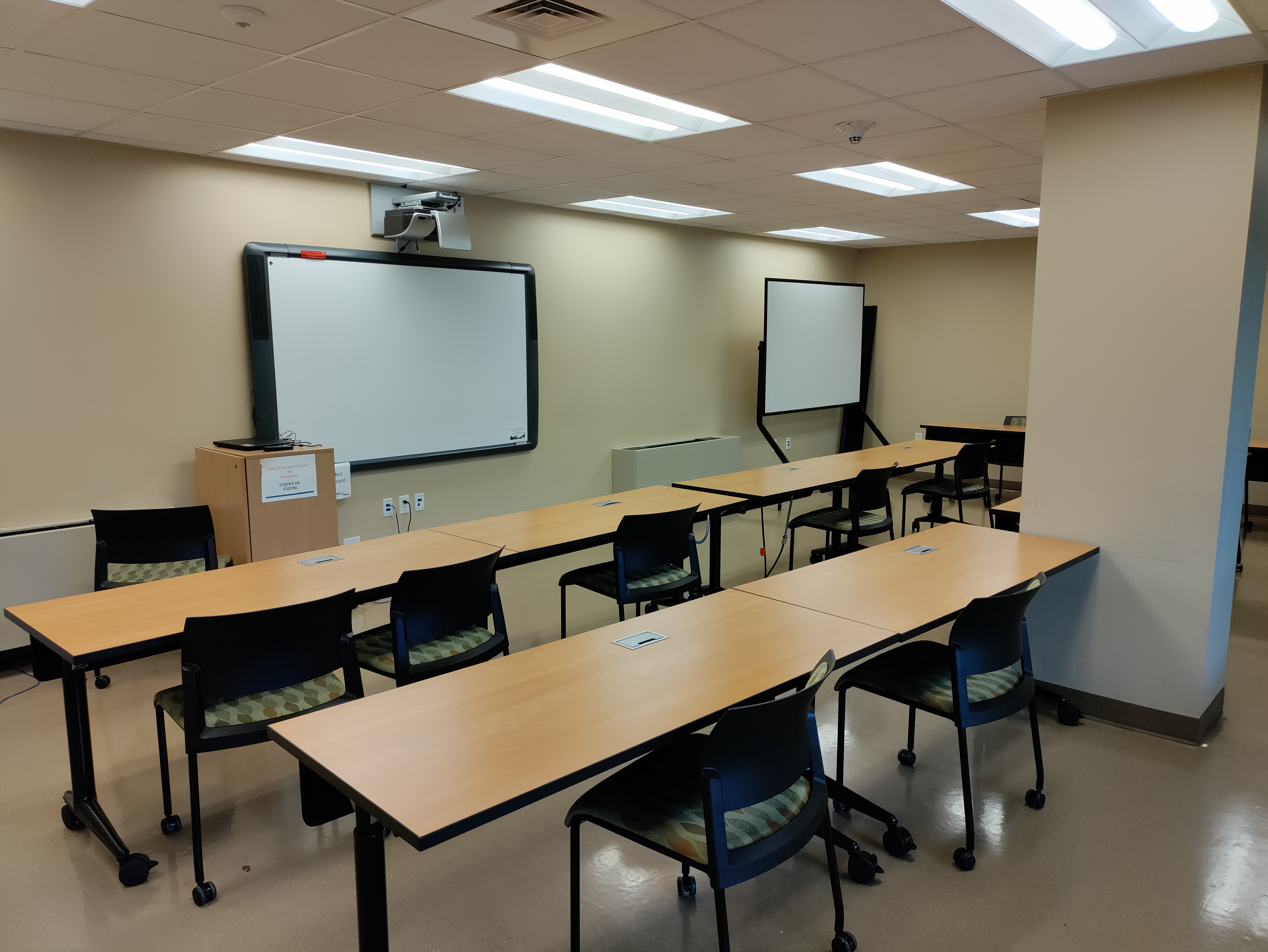 Multipurpose Room 104, the library's downstairs classroom. Chairs and tables face a projector screen and rolling whiteboard.