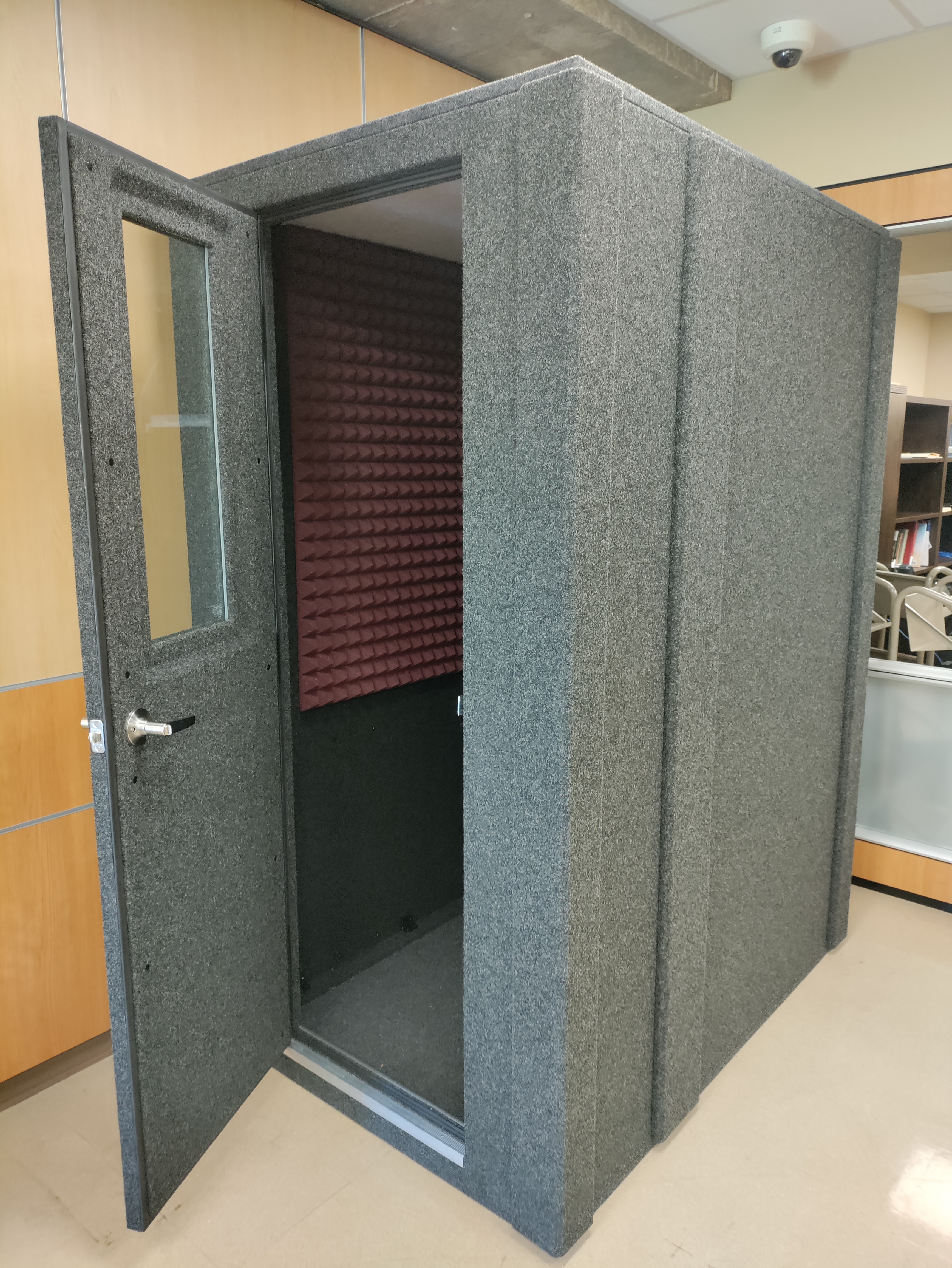 Photo of a freestanding recording booth with the door open. Maroon sound-insulating foam is visible on the inside walls.