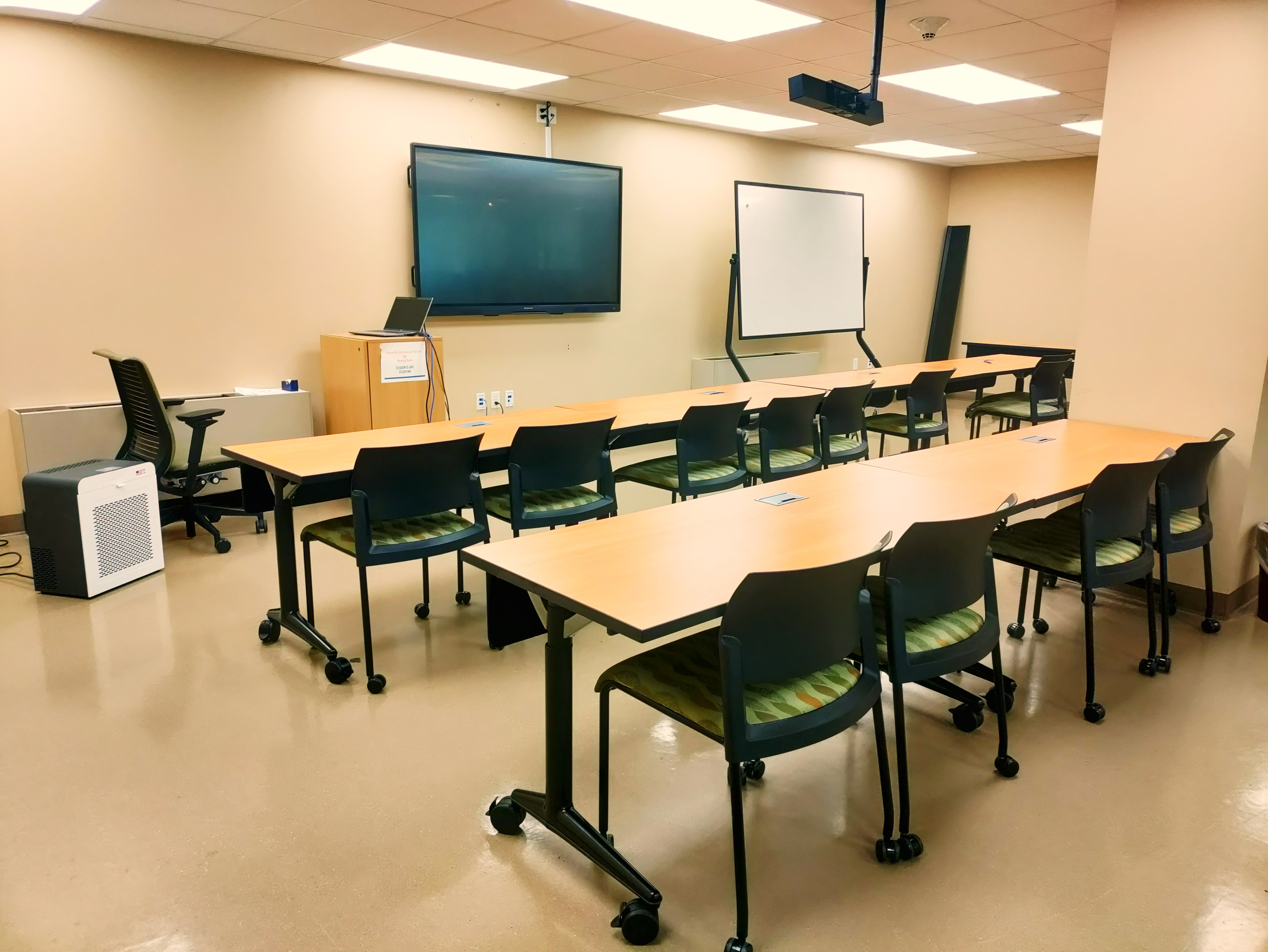 Multipurpose Room 104, the library's downstairs classroom. Chairs and tables face a projector screen and rolling whiteboard.