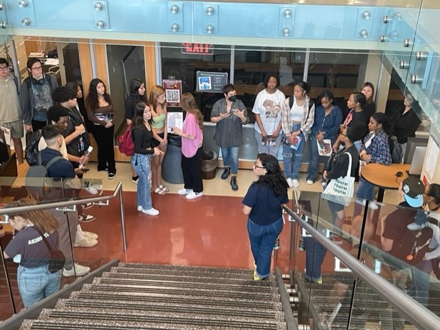 Photo of multiple people on a library tour, seen from above at the top of the library stairs, in front of the multipurpose room.